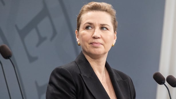 Danish Prime Minister Mette Frederiksen stands in front of two microphones.