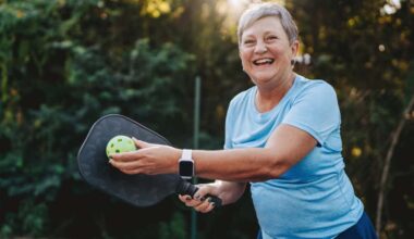 Happy and smiling retiree posing with pickleball and paddle.