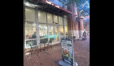Cafe storefront with large glass doors, red awning, and outdoor tables on a brick sidewalk; a menu sign outside.