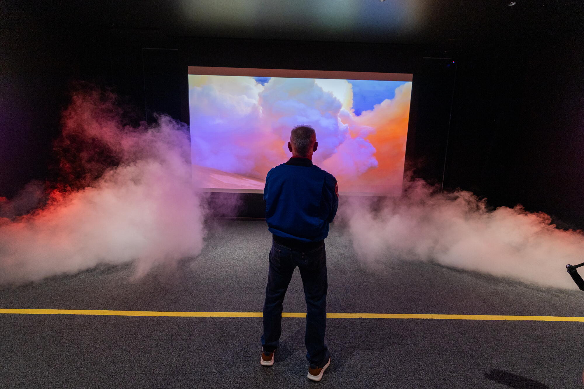 A man stands in front of a screen with smoke billowing dramatically in.