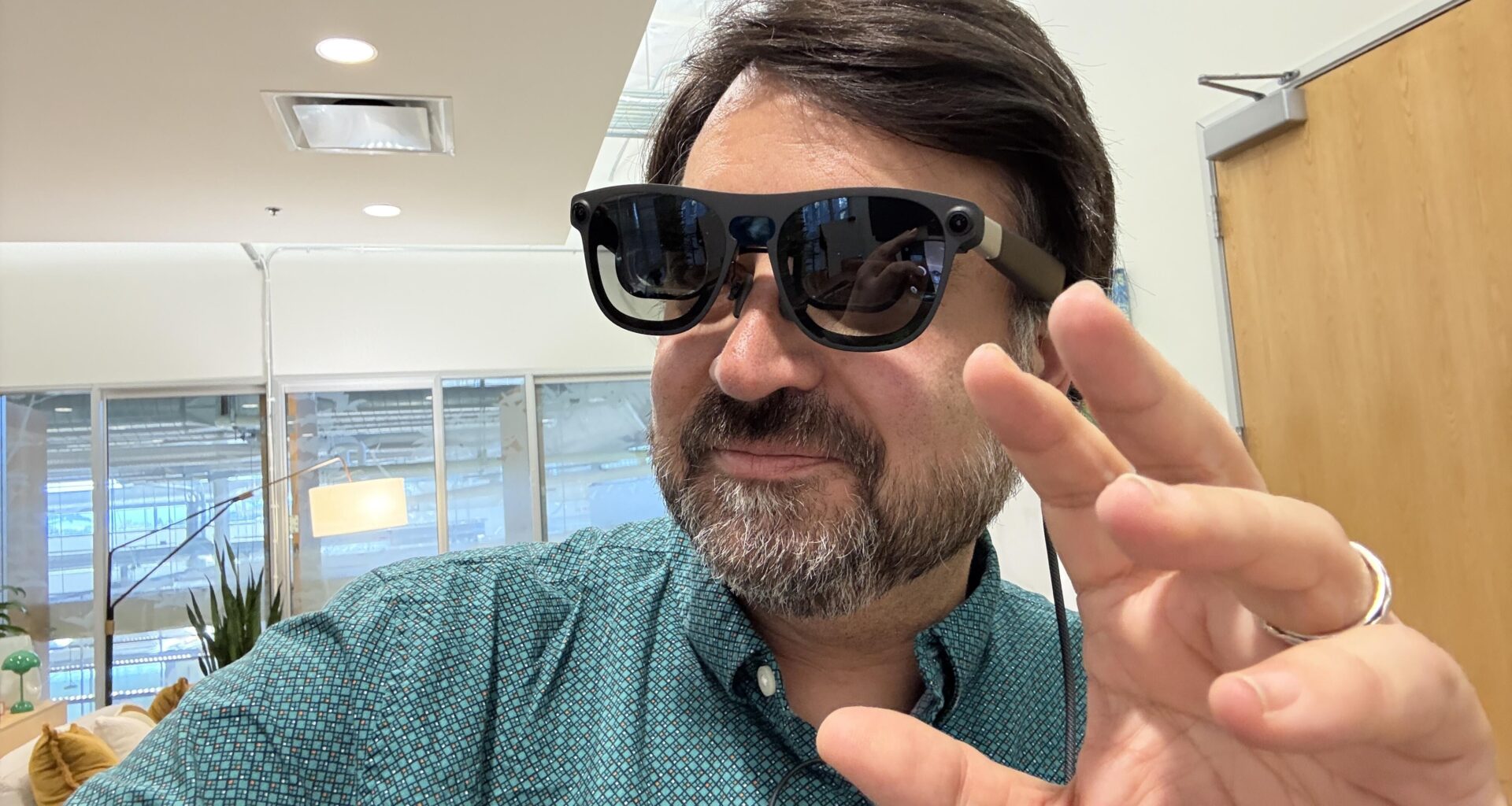 A man wearing Project Aura glasses and gesturing with his left hand.