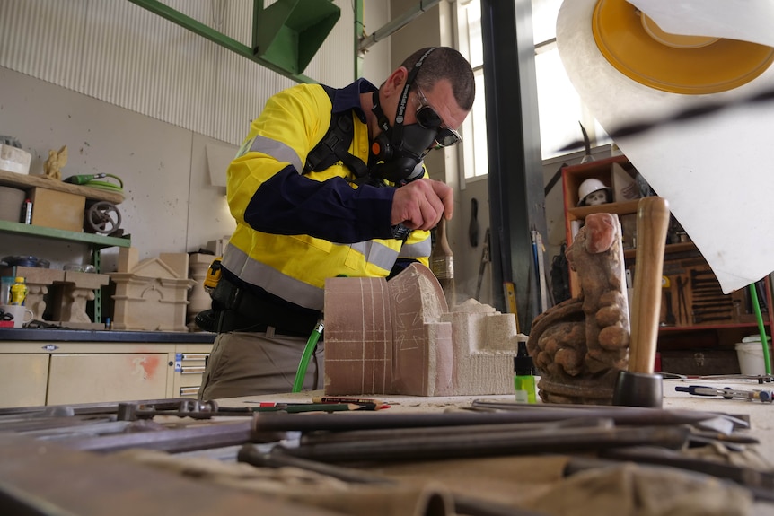a stonemason brushes a sandstone model of a lion atop a crown