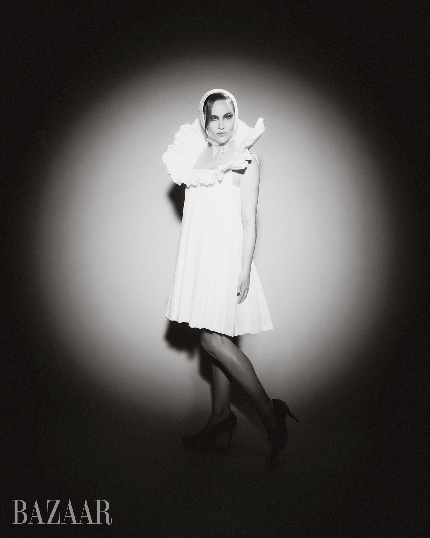A woman in a white dress and ruffled collar poses dramatically in black and white lighting. A woman in a white dress and ruffled collar poses dramatically in black and white lighting.