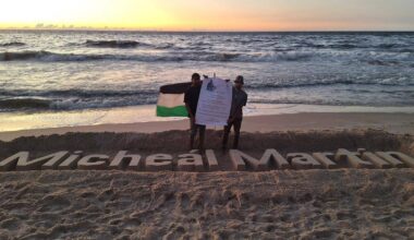 Two Gazan students refused study visas in Ireland pose beside a sculpture of Taoiseach Micheál Martin's name, carved in the sand at Gaza.