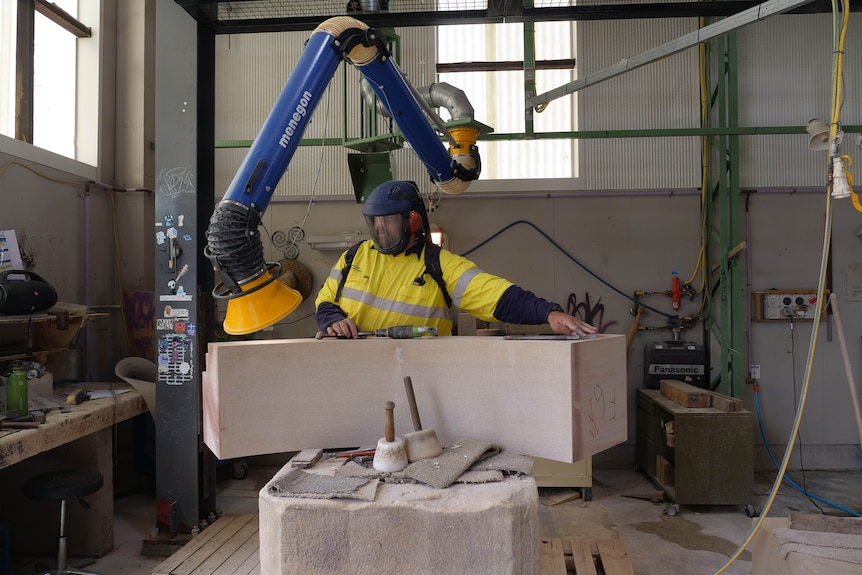 a man at a work station examines a large sandstone block