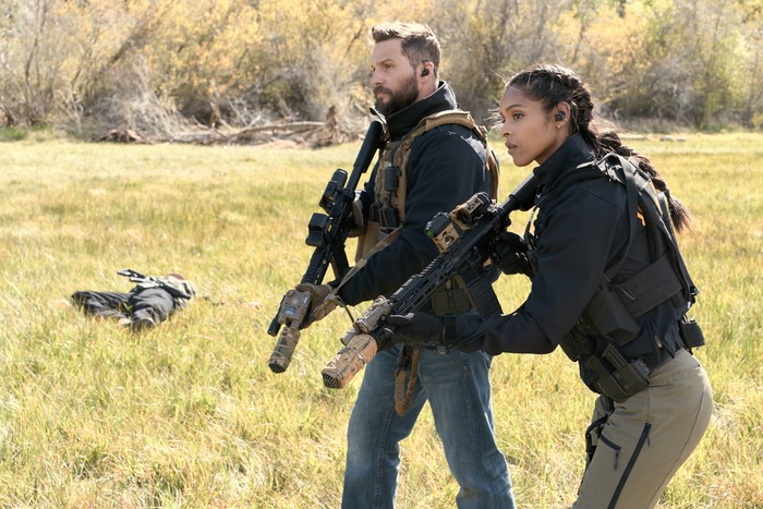 Marshals Season 2 - All Hat No Cattle A man and a woman in full protective gear and assault weapons make their way across afield with their guns drawn.