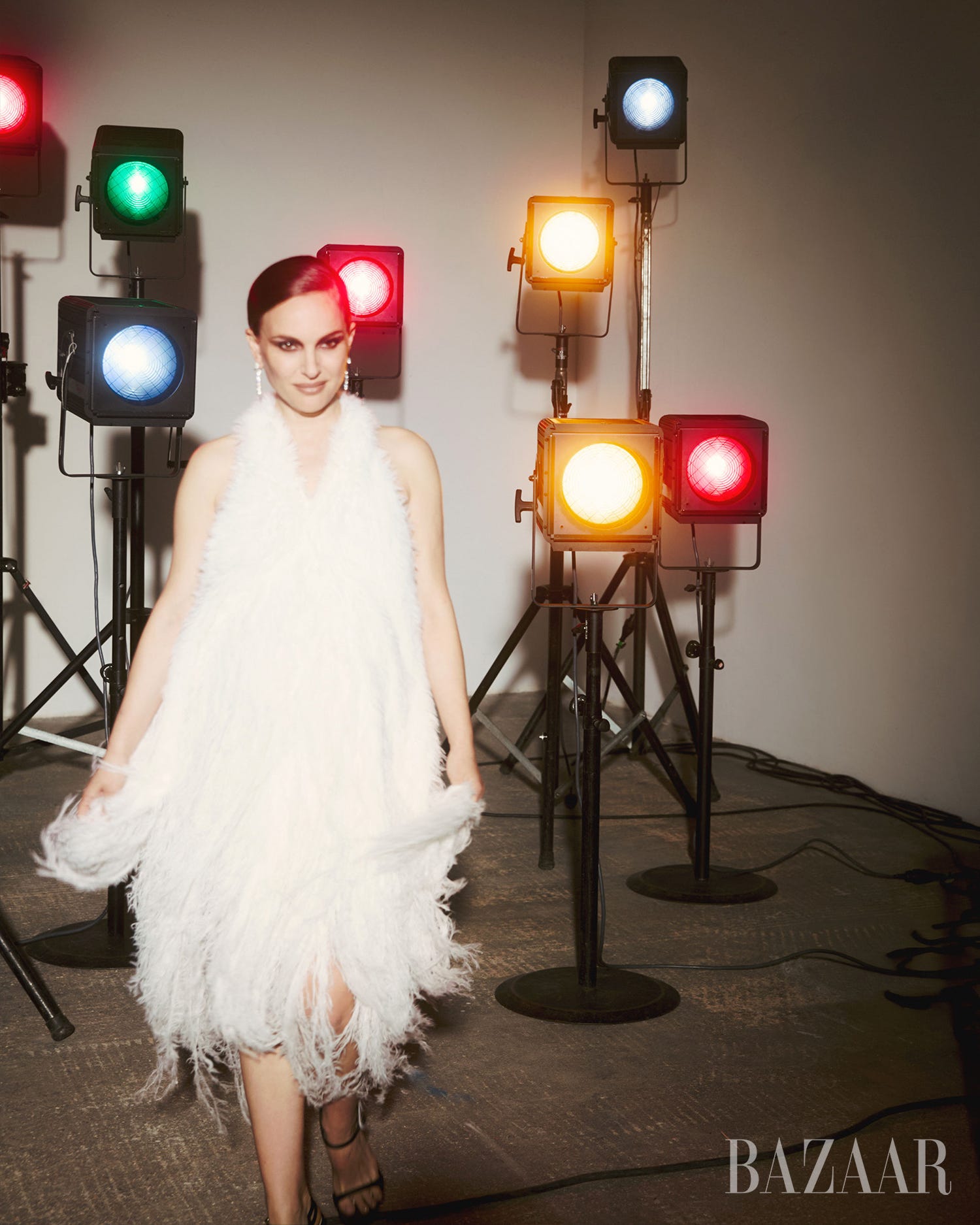 A model in a white feathered dress walks under colorful studio lights. A model in a white feathered dress walks under colorful studio lights.