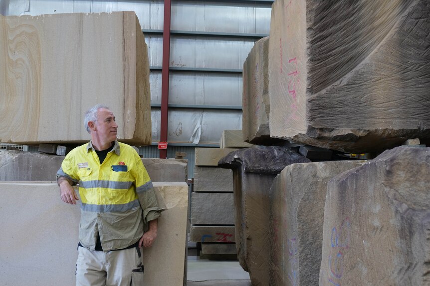 a man leans on a sandstone block next to other large blocks of sandstone
