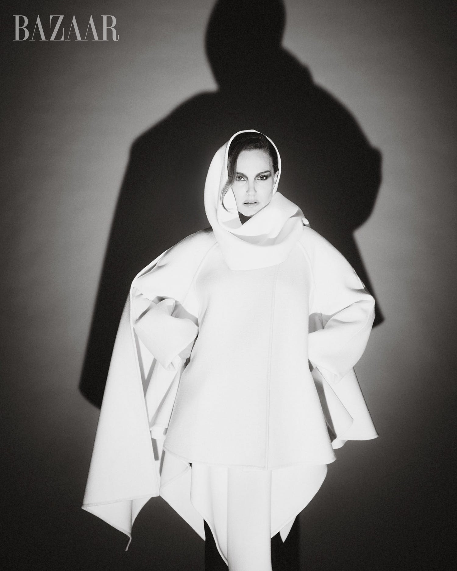 Model posing in a dramatic white outfit with a hood, casting an intriguing shadow against a dark backdrop. Model posing in a dramatic white outfit with a hood, casting an intriguing shadow against a dark backdrop.