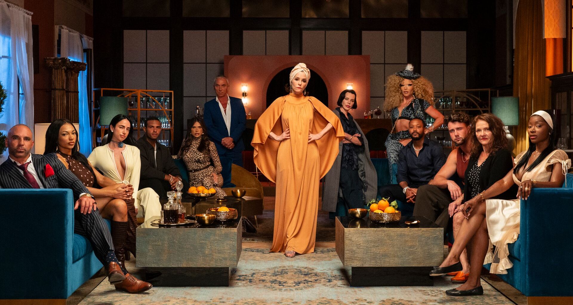 parker posey poses in front of the reality tv contestants appearing on hulu's the mob as they sit in chairs and stand around her in a promotional shot