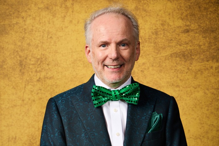 Nick Park in front of a gold background, wearing a tuxedo and green bow tie.