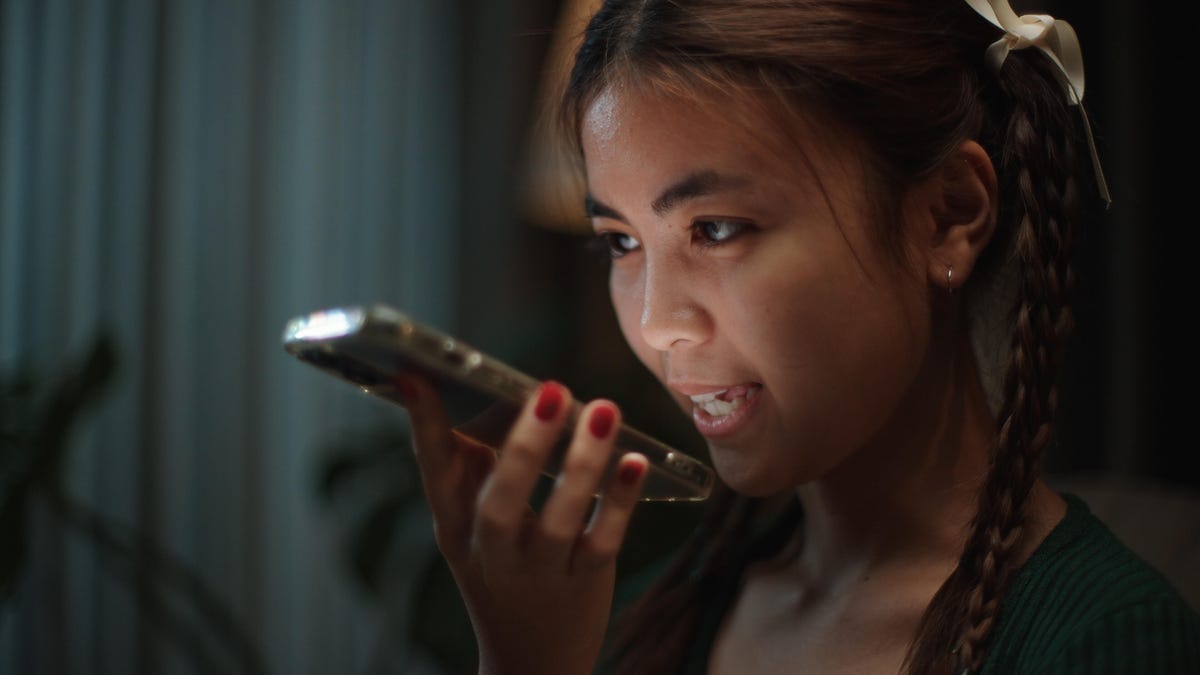 A young woman talks on a cellphone, her face illuminated by the glow of the phone screen.