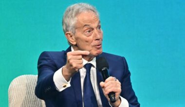 Tony Blair speaks into a microphone, gesturing with his hand during a panel discussion at the Austrian World Summit.