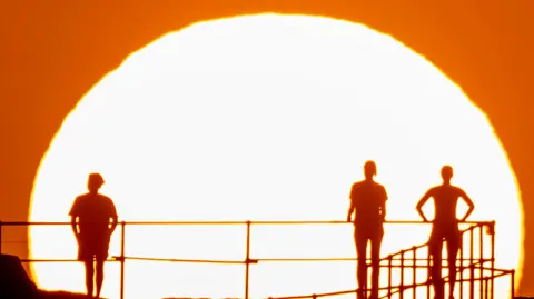 Getty Images Three people watch the Sunrise in Sydney, Australia last November amid a strong ongoing heatwave