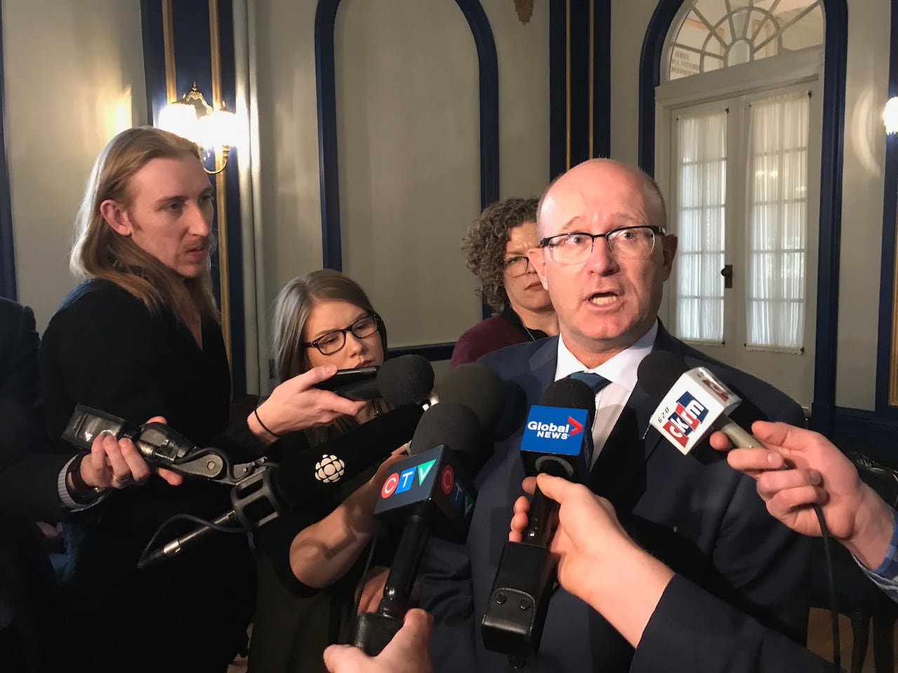 A politician with glasses speaks in front of a media scrum and reporter's microphones 