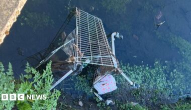 A trolley half buried in mud on the river Usk. the picture is taken through railings.