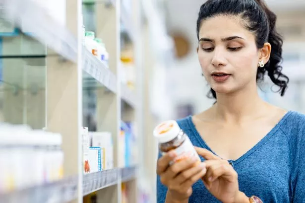 A female Indian customer reading labels medicine the side of the bottle bottle on the shelves of a pharmacy.