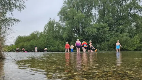 FLOW CIC A group of wild swimmers walking out into the river at Fordingbridge