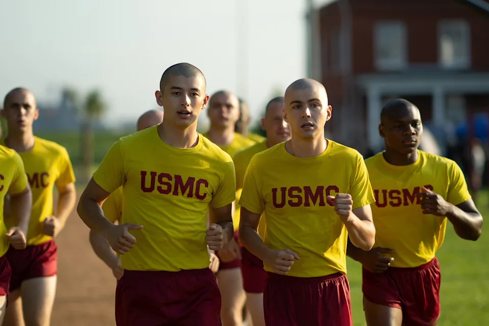 Marine recruits in yellow "USMC" shirts running together on a training track