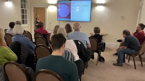 FLOW CIC representative, Maddie Crabb, giving a presentation at the front of a collection of groups and members of the public on Quakers House in Salisbury