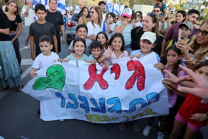Children hold a sign that reads, "Guy, we've missed you, welcome back," as freed hostage Guy Gilboa-Dalal returns home to the settlement of Alfei Menashe, on Sunday.