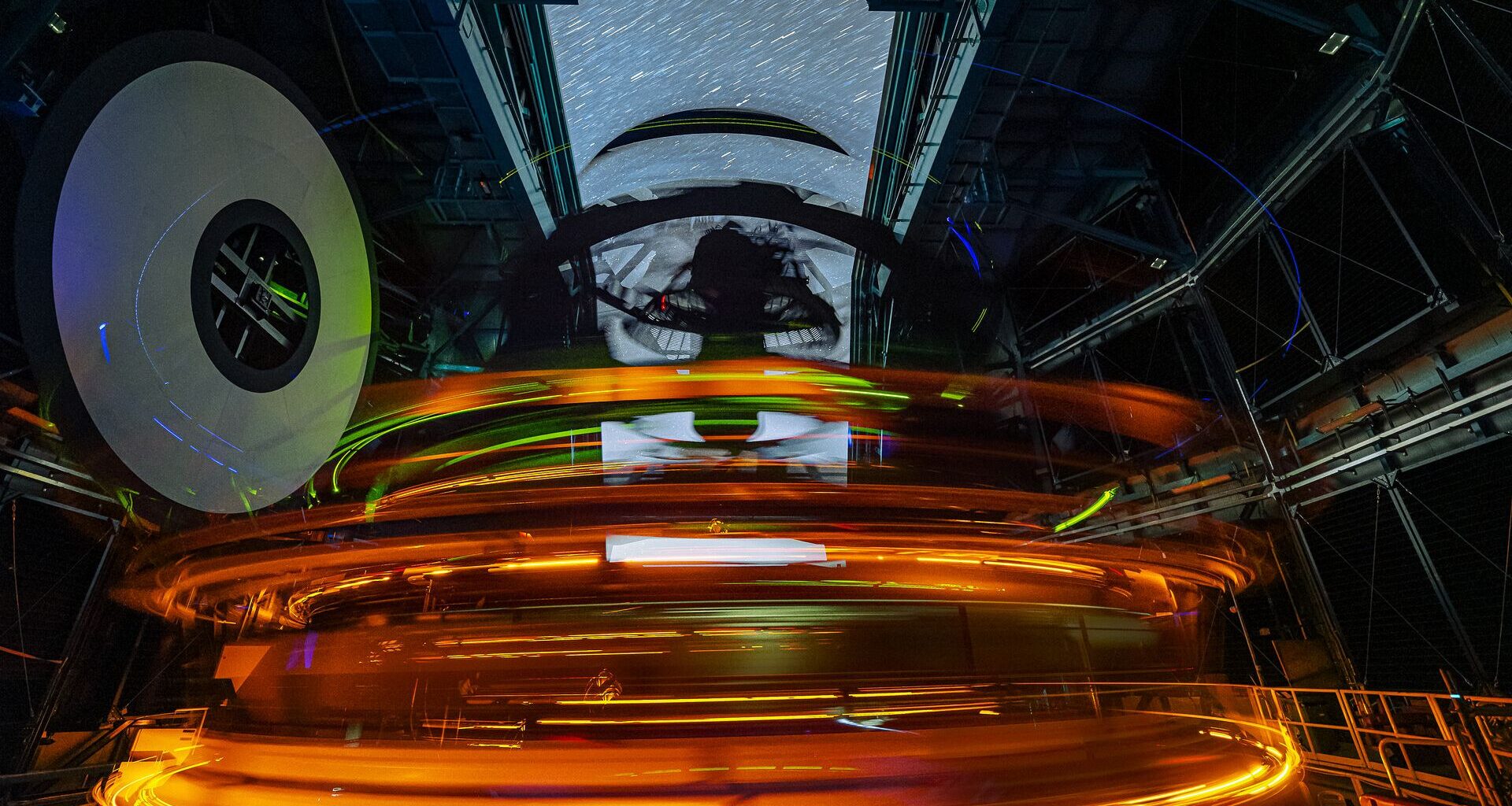 A long exposure image shows rings of glowing lights inside the dome of an observatory with streaks through the open dome showing the stars