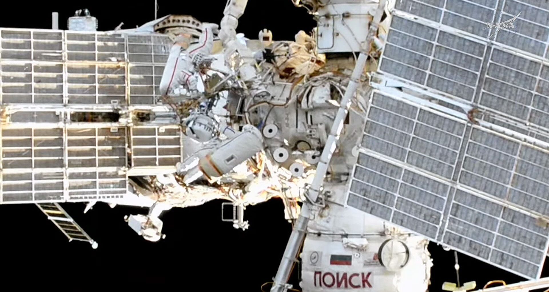 an exterior view of a space station includes two spacesuited cosmonauts at work during a spacewalk