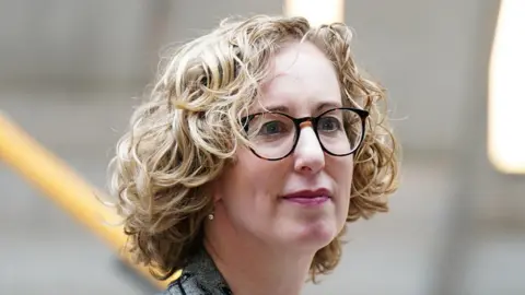 PA Media Lorna Slater has blonde, curly hair and is wearing glasses and a grey jacket