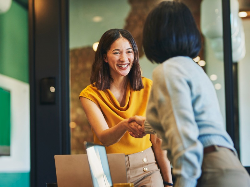 Cheerful businesswomen shaking hands in meeting room