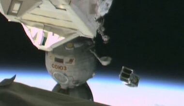 A small metal satellite is launched floating above Earth with part of the International Space Station seen on the left part of the image