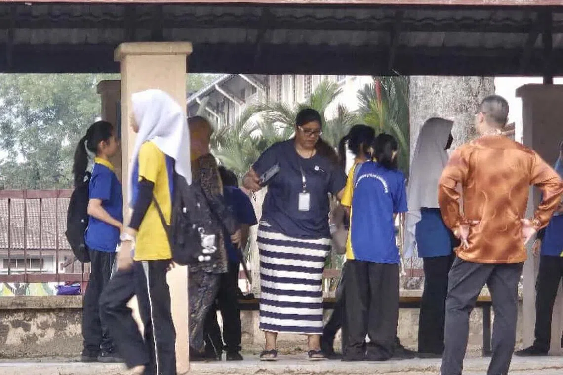 A teacher from SMK Bandar Utama Damansara 4 uses a metal detector to screen students before they enter the school compound