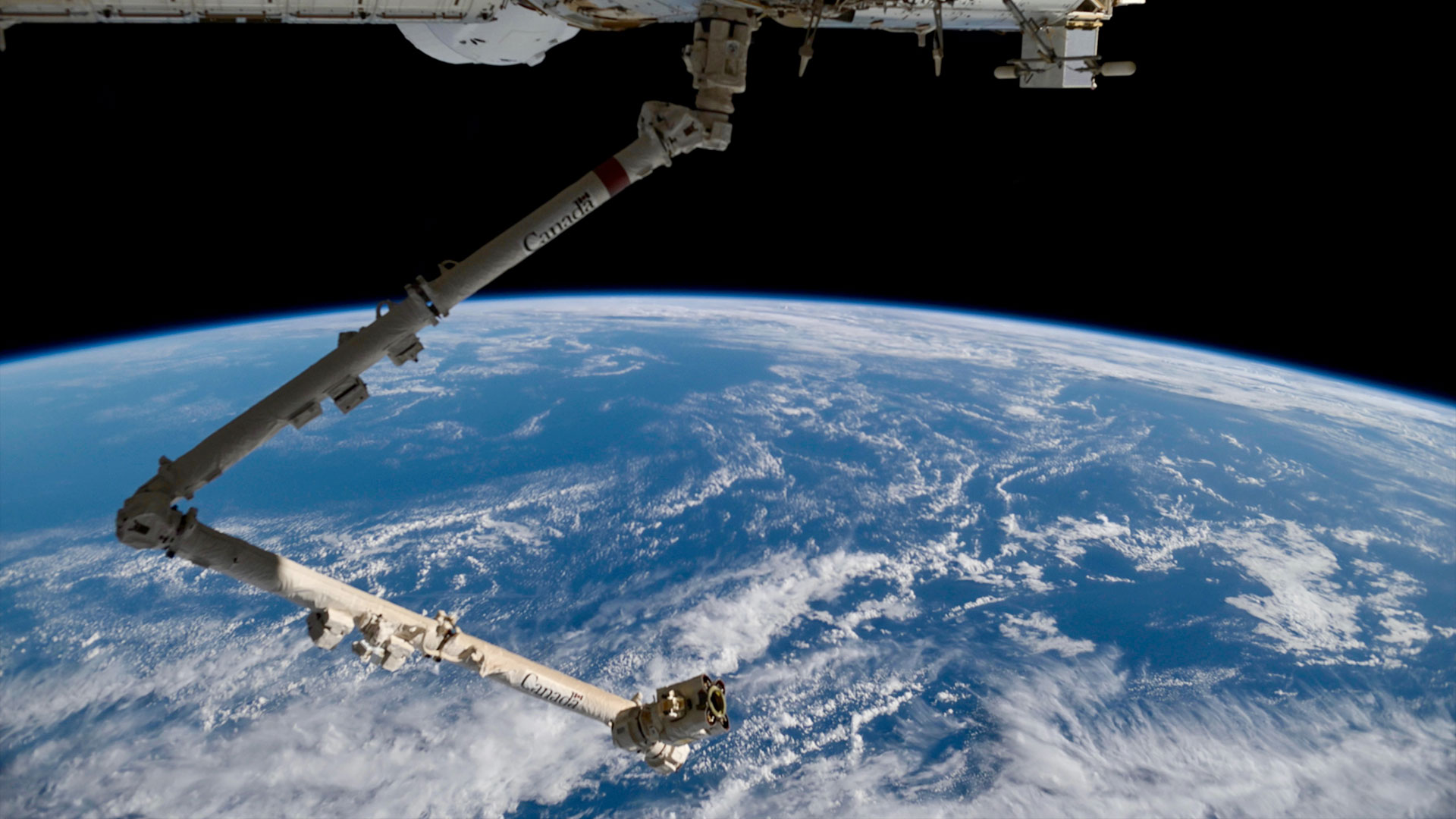 a large robotic arm extends from a space station over the horizon of a blue and white planet