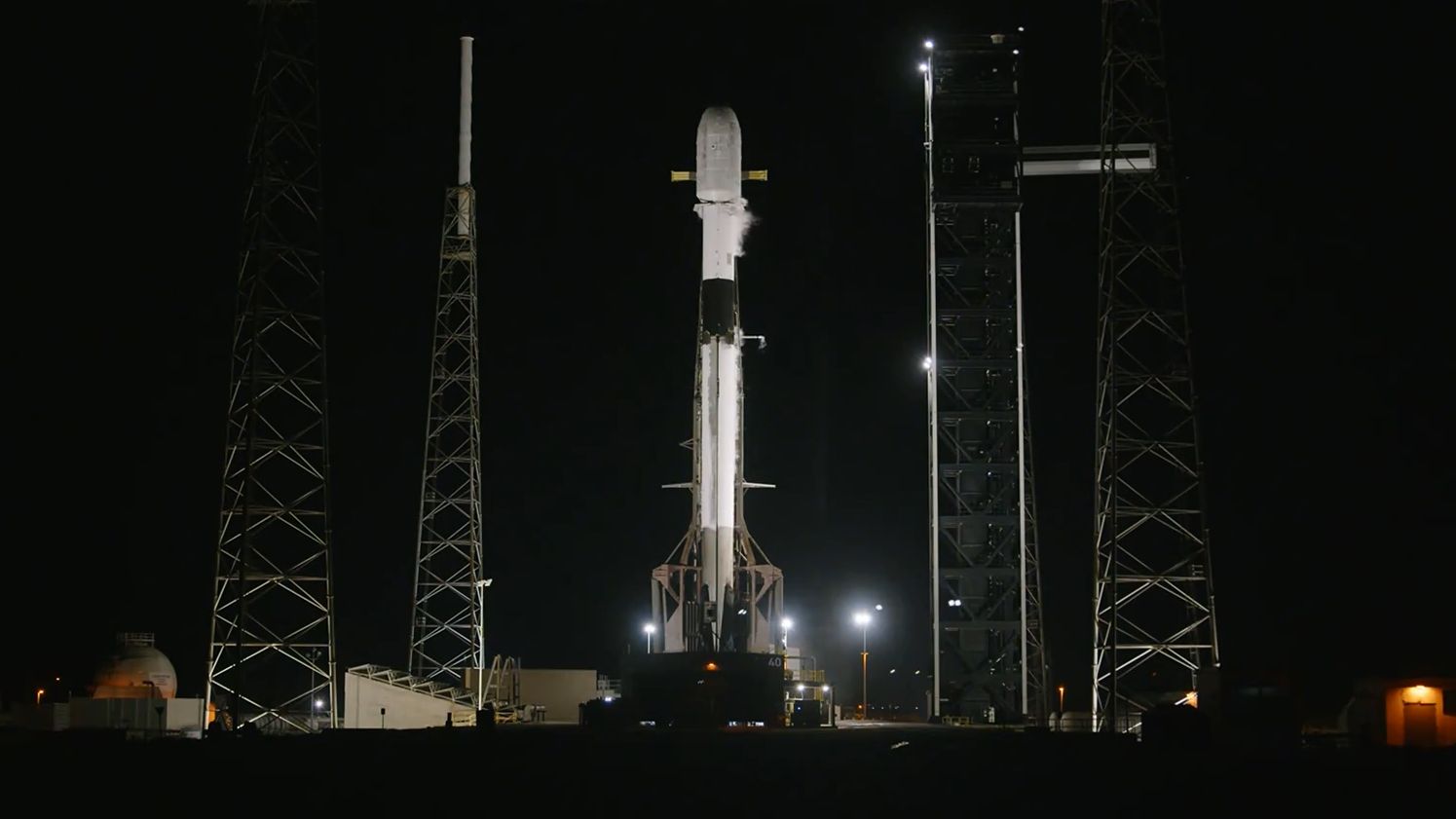 A SpaceX Falcon 9 rocket standing fully fueled on a launch pad at night.