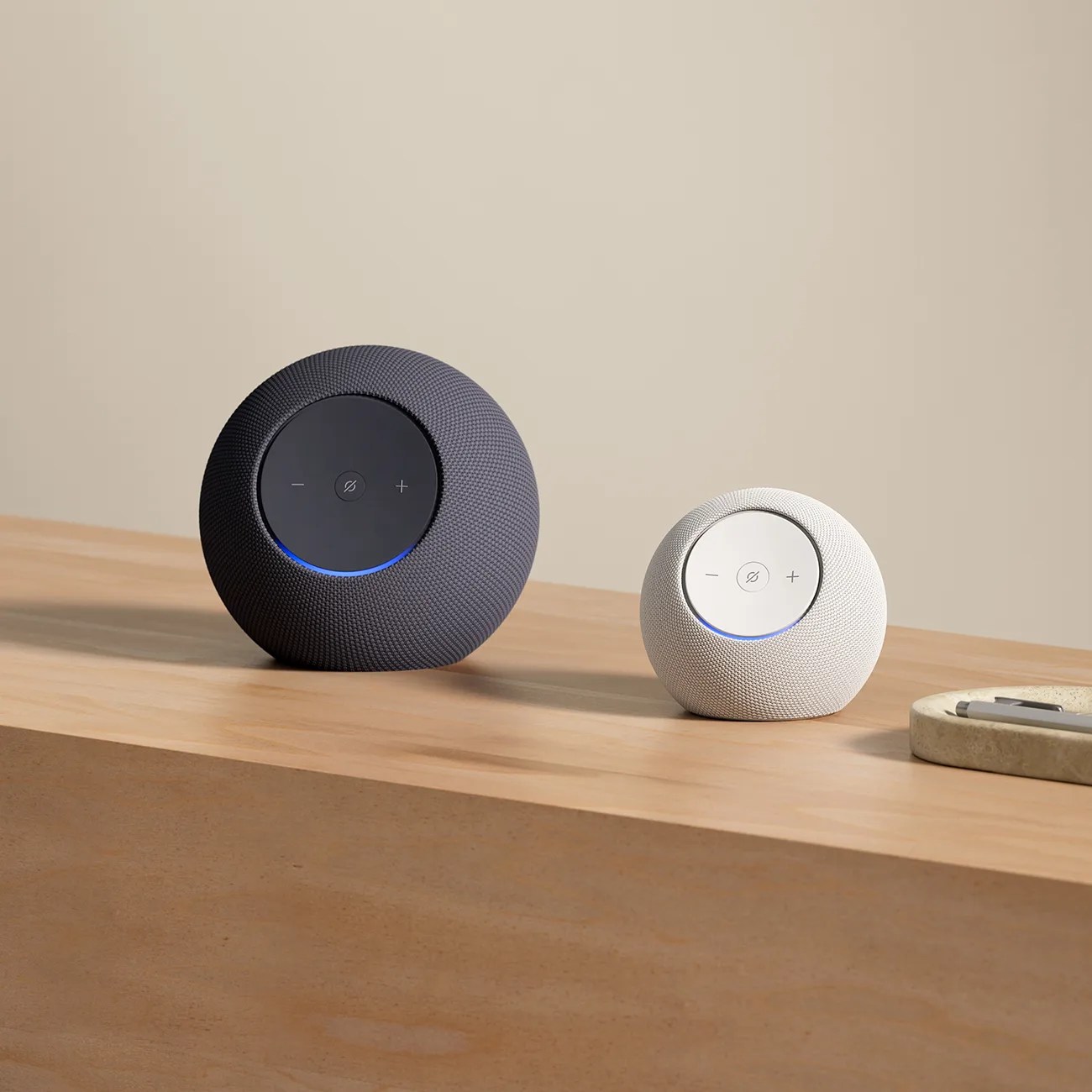 Two round smart speakers, one black and one white, with volume and mute buttons on top, placed on a wooden surface.