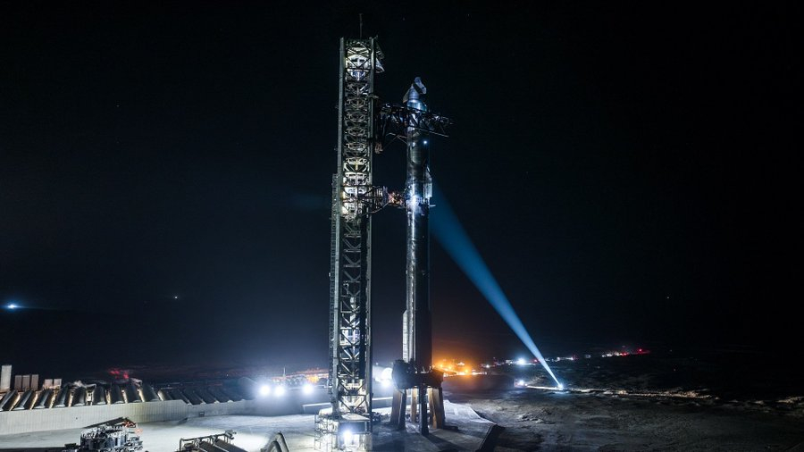 A silver winged Starship stands atop its giant boster for SpaceX Flight 8