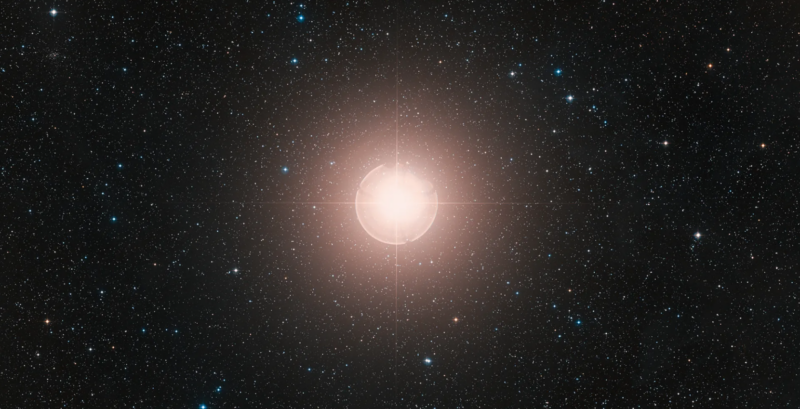 Bright orangish star at center with surrounding glow and other stars in the background.