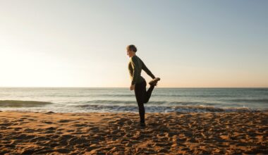 Woman holding one leg standing on the beach next to the sea