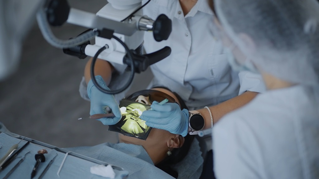 Dentist performing a detailed orthodontic procedure under magnification, patient lying in a dental chair, illuminated treatment area visible