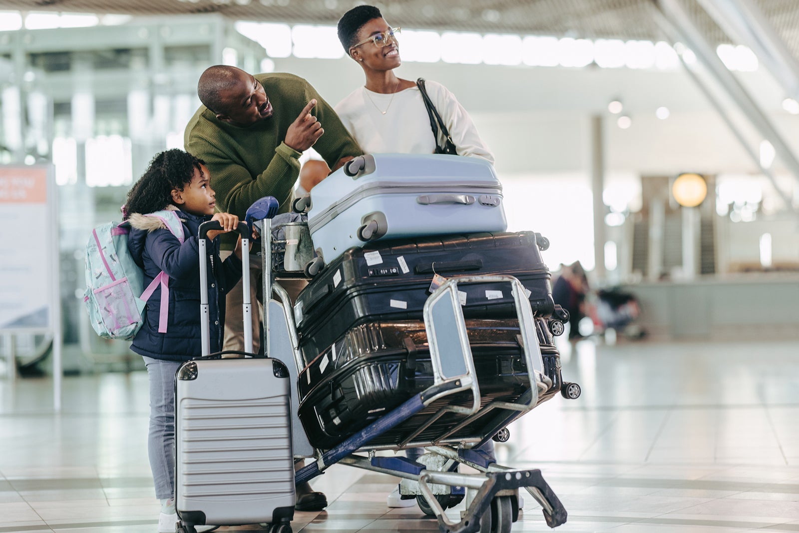 A family at an airport with a cart of luggage