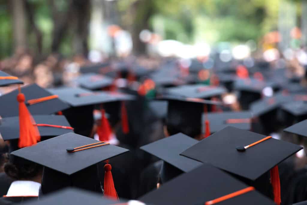 A large group of Leadership Louisiana graduates wearing black caps with red tassels stand closely together at an outdoor graduation ceremony.