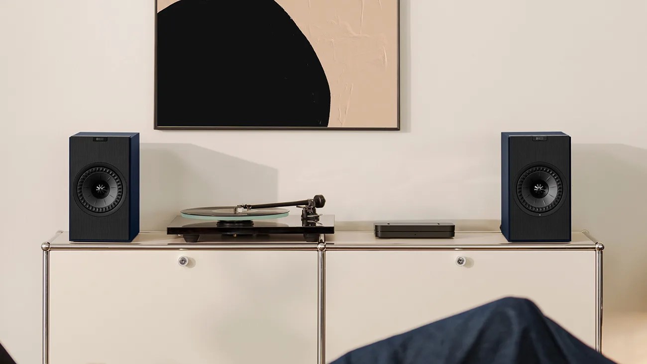 Pair of black bookshelf speakers on a white cabinet with a turntable and audio device between them.