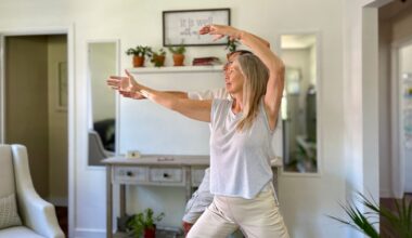 woman standing in front of a man both performing tai chi moves in a living room setting looking sideways away from the camera