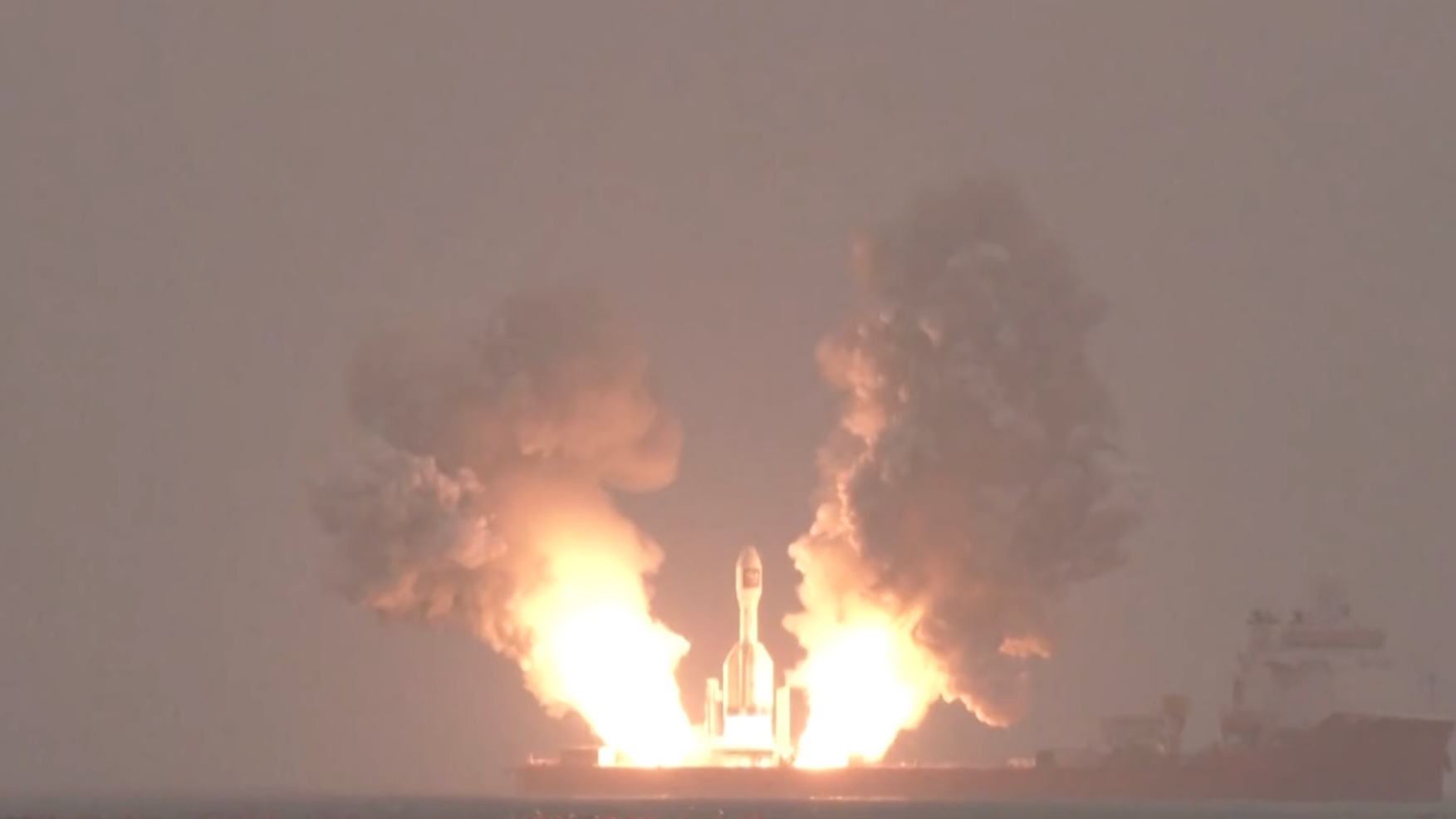 a squat white rocket launches from a ship at sea, generating two huge plumes of exhaust