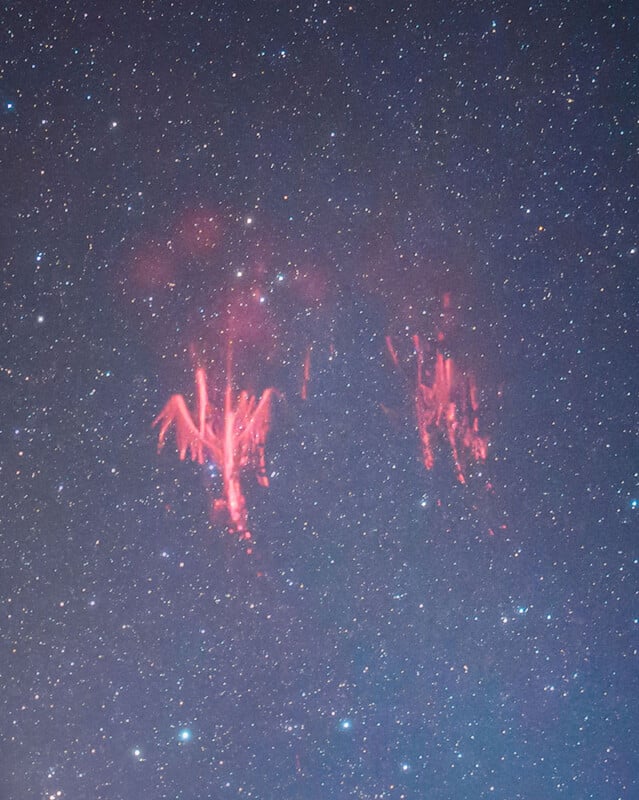 A night sky filled with stars features bright, reddish, tentacle-like lightning formations known as red sprites, illuminating the upper atmosphere.