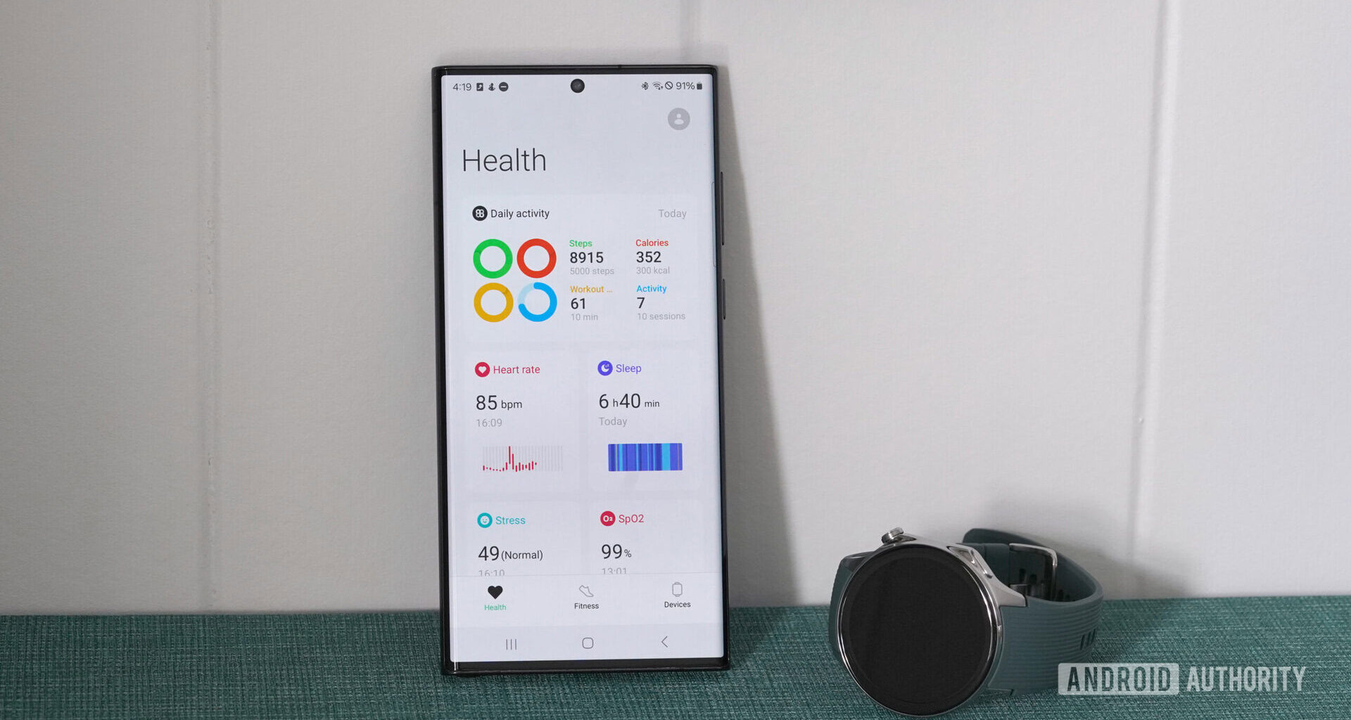 A OnePlus Watch 2 rests next to a Samsung Galaxy S22 Ultra displaying a user's health stats in the OHealth app.