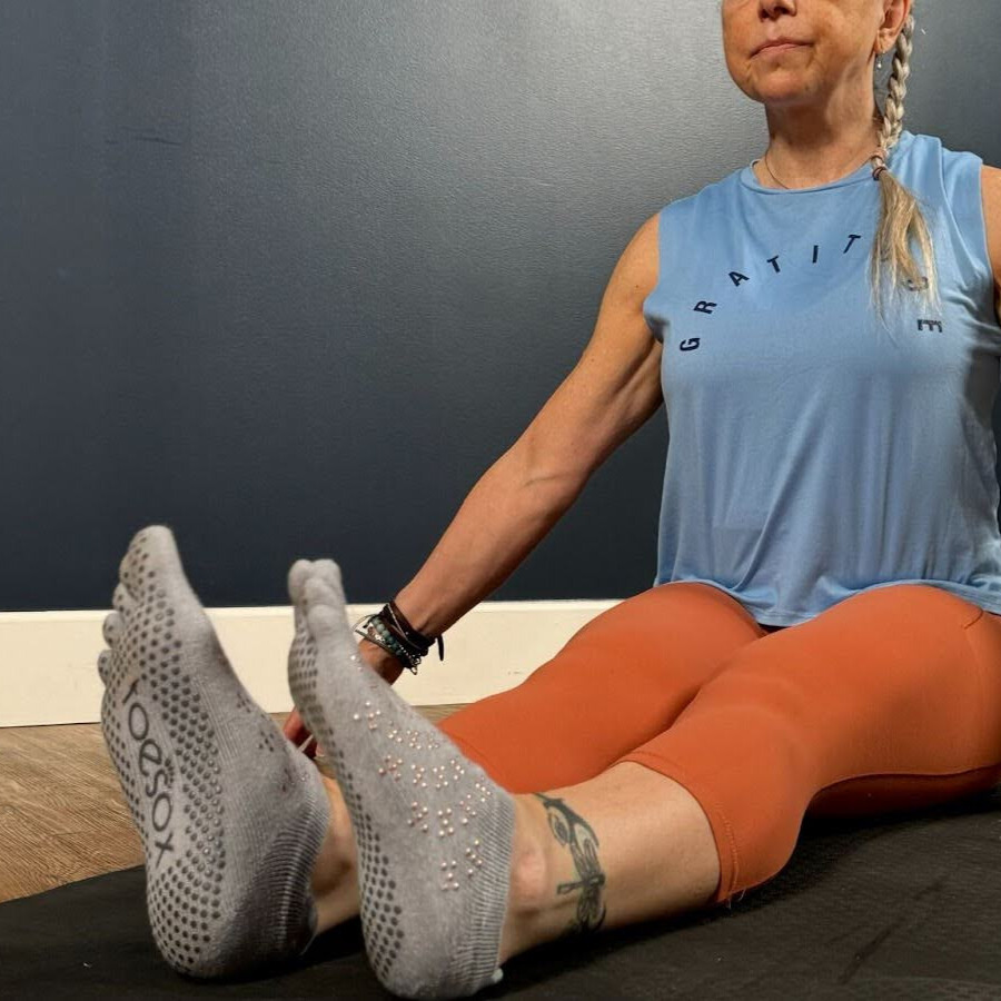 Woman sits cross-legged on mat demonstrating wrist movement