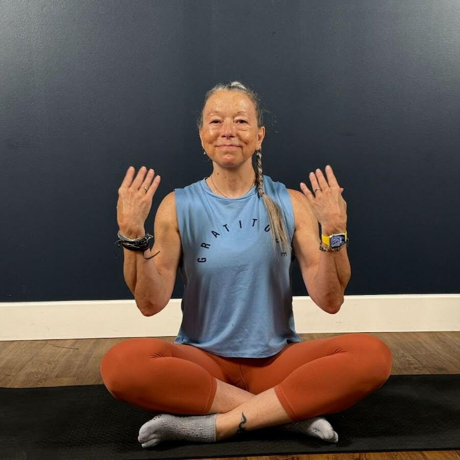 Woman sits cross-legged on mat demonstrating wrist movement