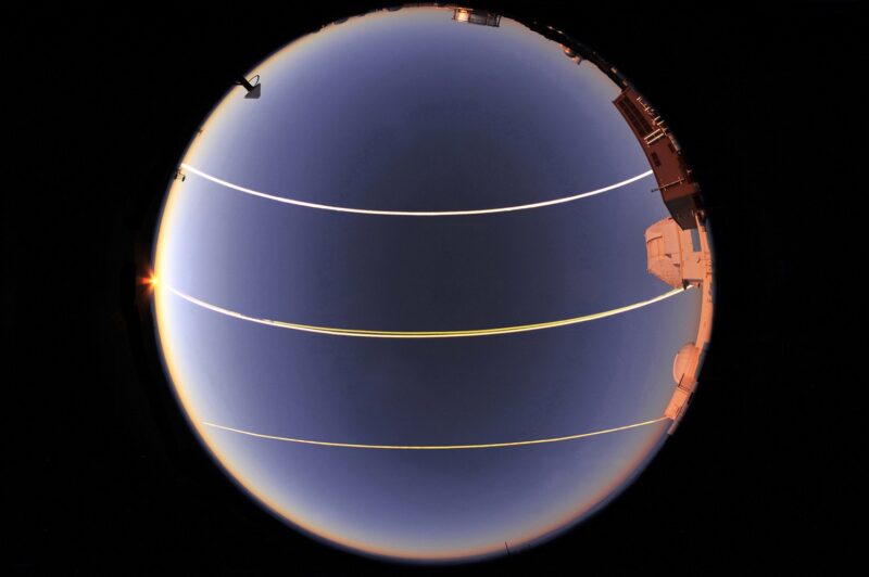 Fisheye view of sky with three bright parallel lines across it.