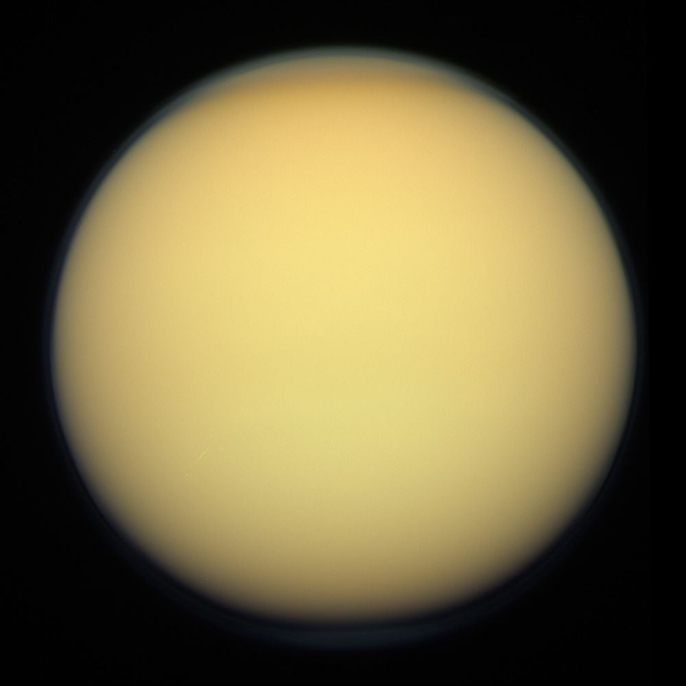 This Cassini image of Titan has become iconic. The moon's thick organic atmosphere blocks visible light, limiting our attempts to understand its surface chemistry. Image Credit: By NASA/JPL-Caltech/SSI/Kevin M. Gill - File:Titan - December 16 2011 (40047599334).jpg by [1], CC BY 2.0, https://commons.wikimedia.org/w/index.php?curid=125680346