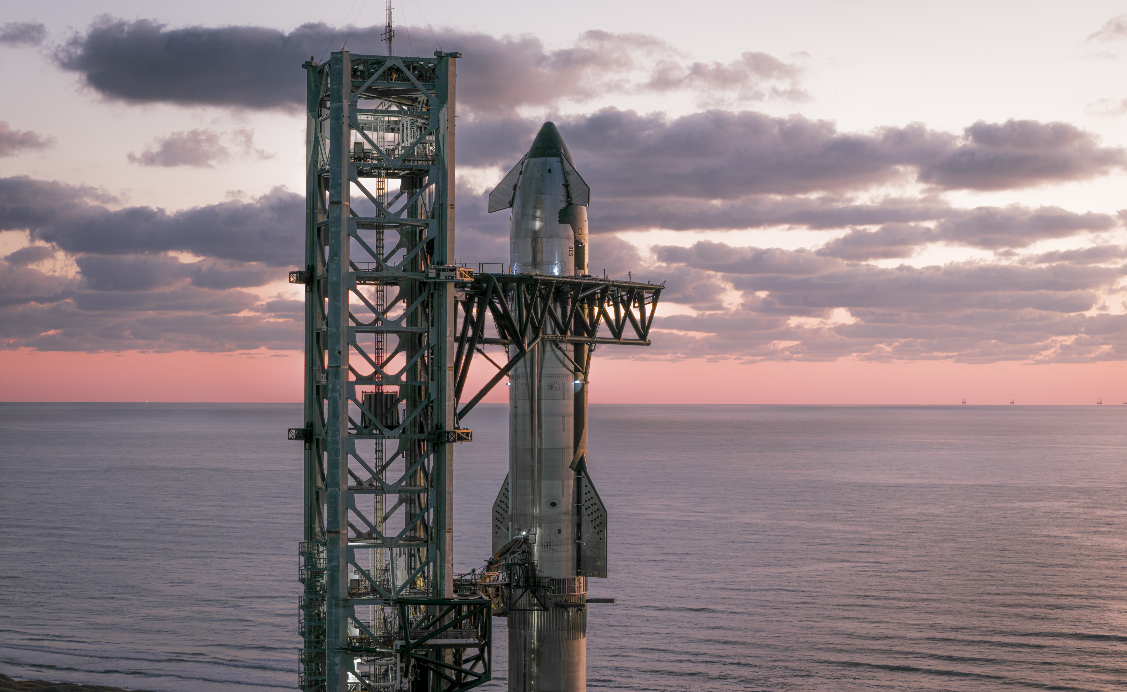 A SpaceX Starship rocket atop its booster with the Gulf of Mexico in the distance and a sunset sky.